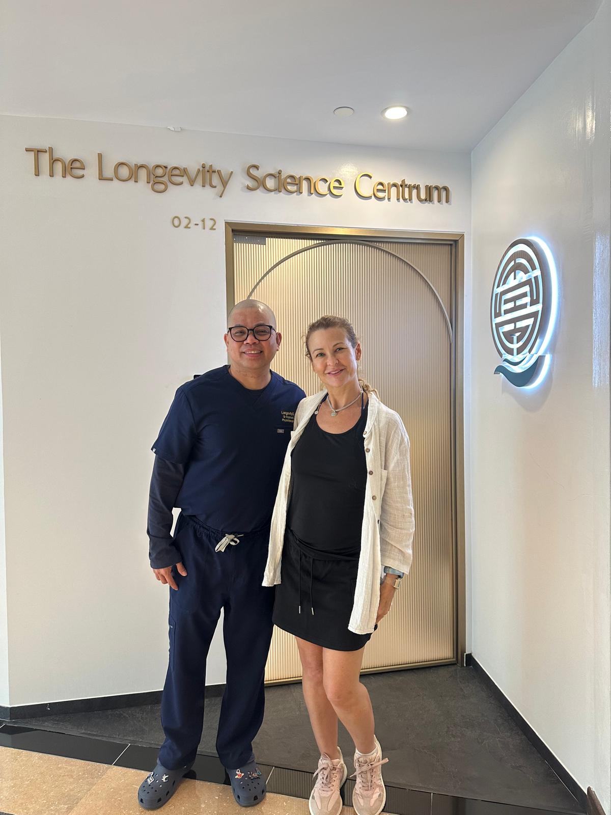 A team member and a guest together at The Longevity Science Centrum's entrance, in front of the clinic door and glowing logo.