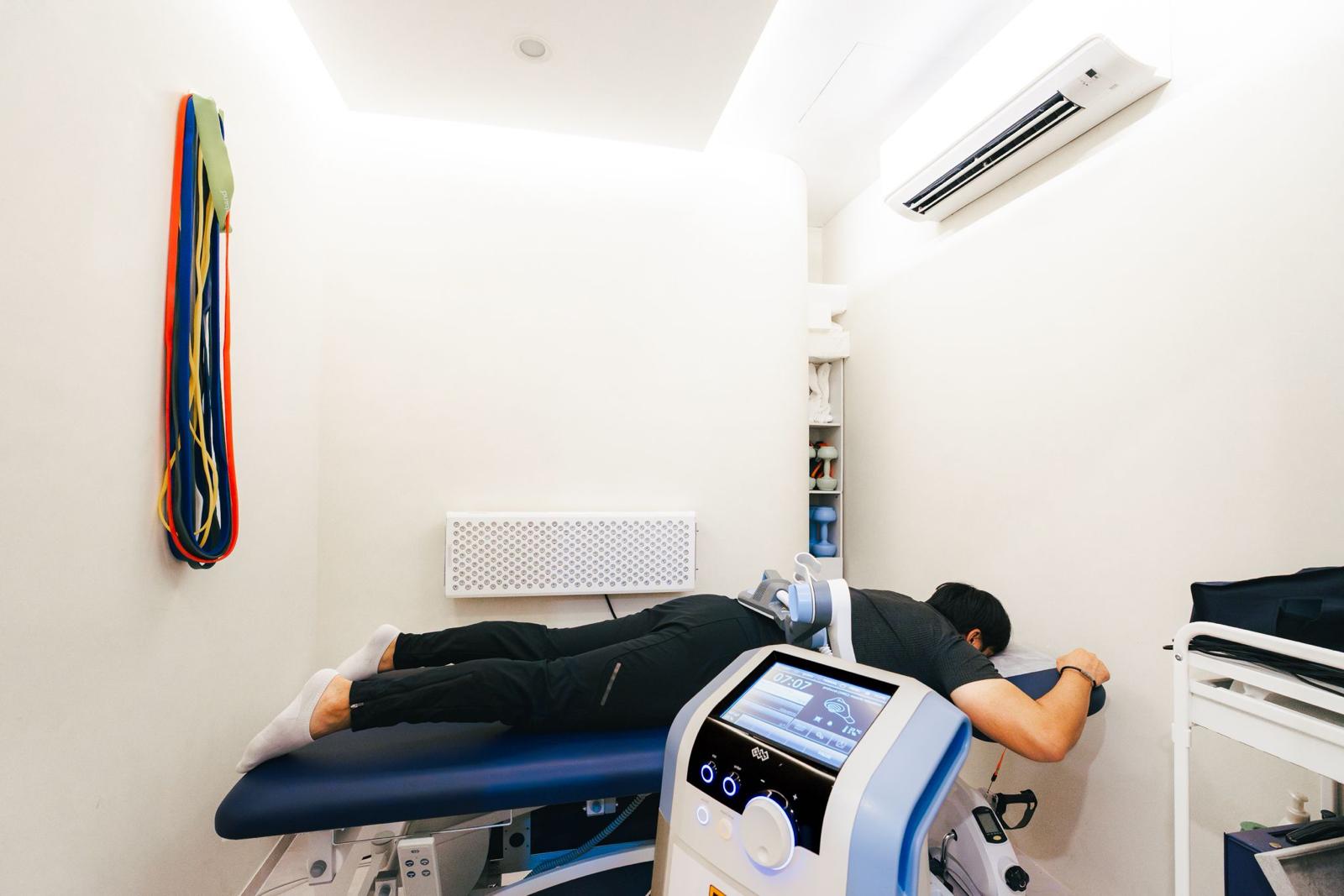 A client lying face down on the treatment couch beside the shockwave therapy console at The Longevity Science Centrum.