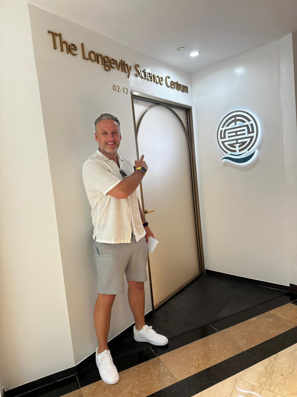 A guest pointing to The Longevity Science Centrum's name in gold lettering at the clinic entrance.