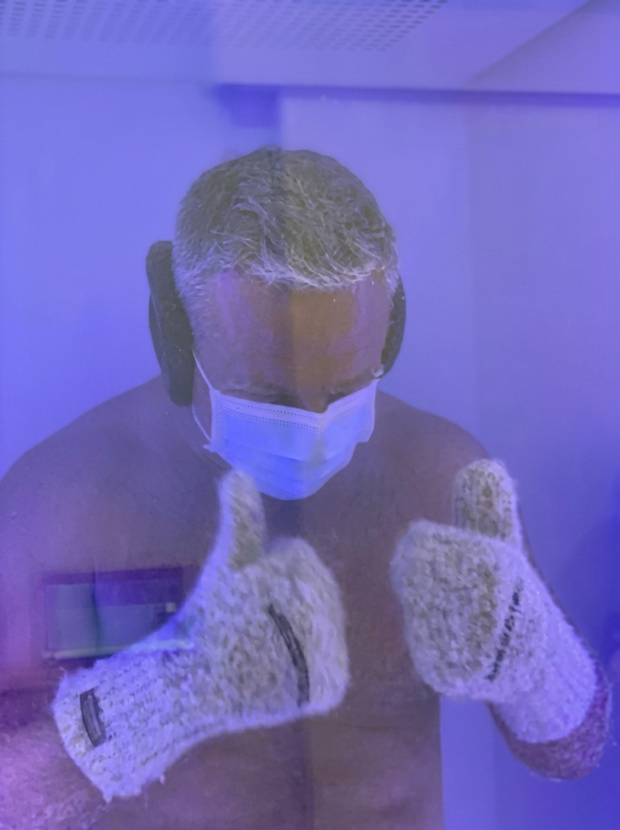 A guest inside the whole-body cryotherapy chamber at The Longevity Science Centrum, wearing a face mask and protective gloves in the blue-lit cabin.