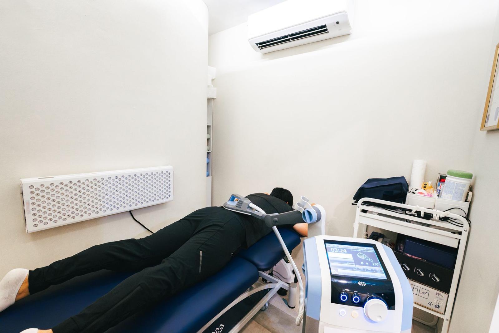 A guest lying on a treatment couch receiving body recovery therapy in a bright treatment room at The Longevity Science Centrum.