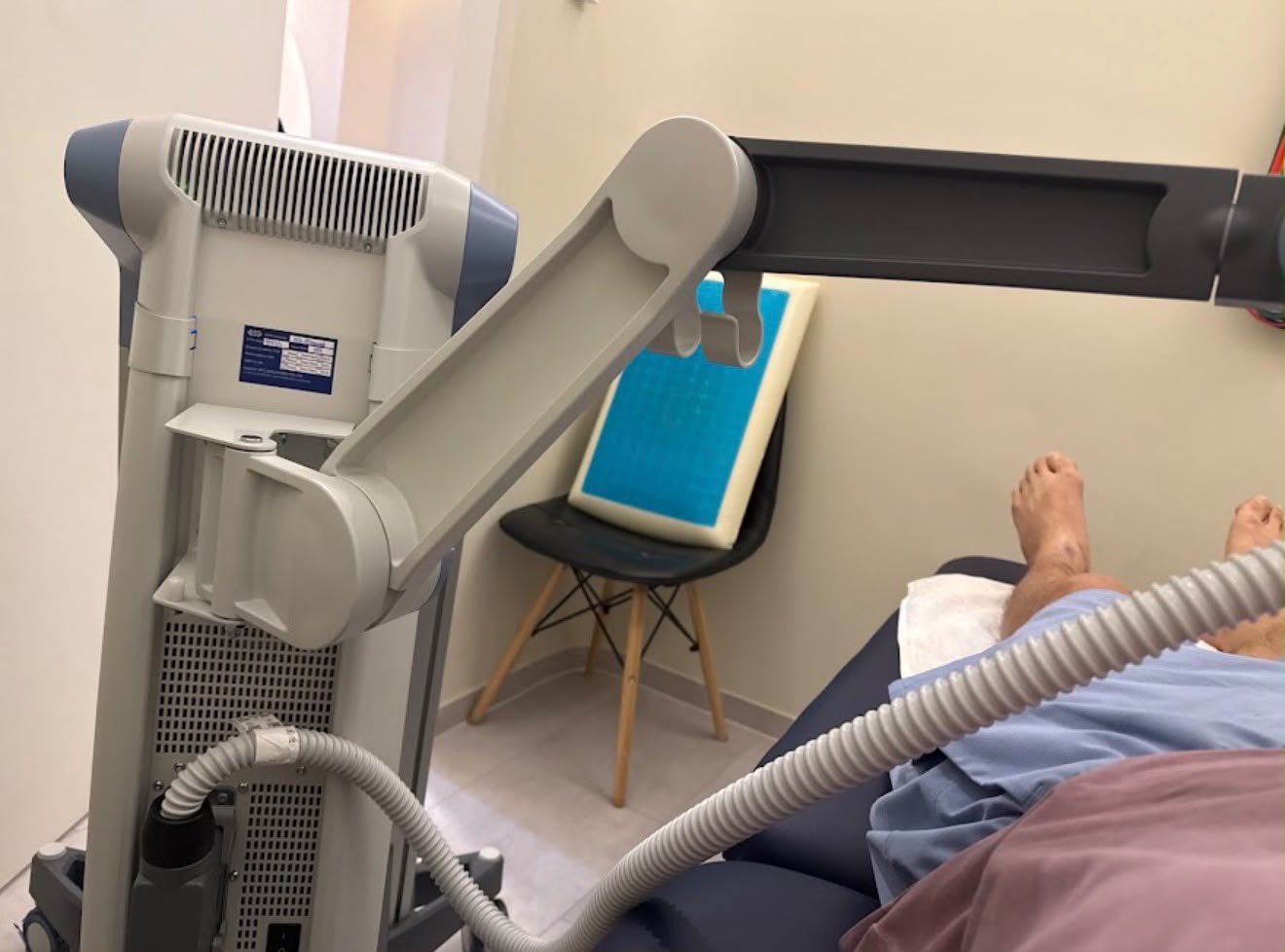 A client on a treatment couch receiving high-intensity pulsed electromagnetic field therapy, the device's articulated applicator arm positioned over their leg at The Longevity Science Centrum.