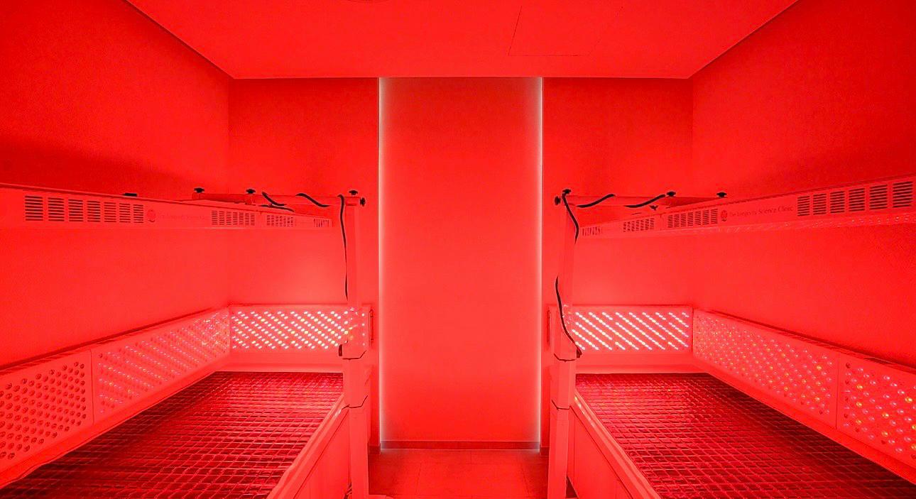 The photobiomodulation therapy room at The Longevity Science Centrum, lit deep red by full-body LED panels on either side of a central column.