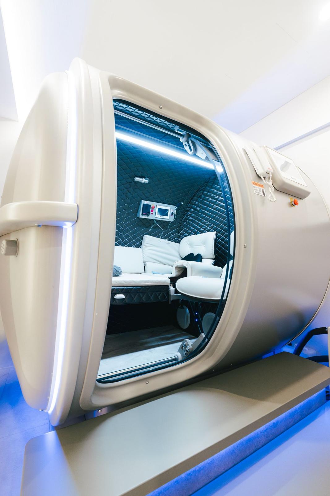 The hyperbaric oxygen chamber with its door open, quilted interior lit by cool blue light.