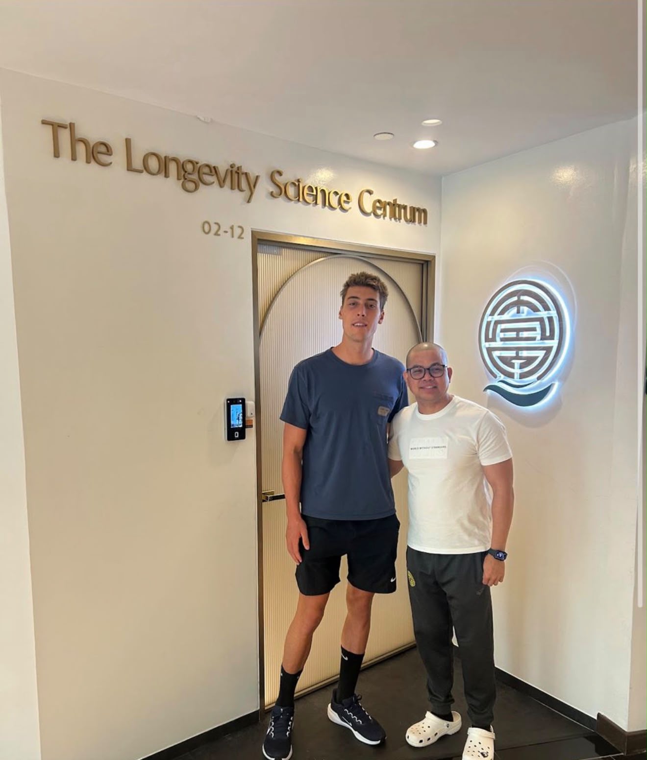 A guest and a team member together beneath The Longevity Science Centrum's name in gold lettering, beside the glowing clinic emblem.