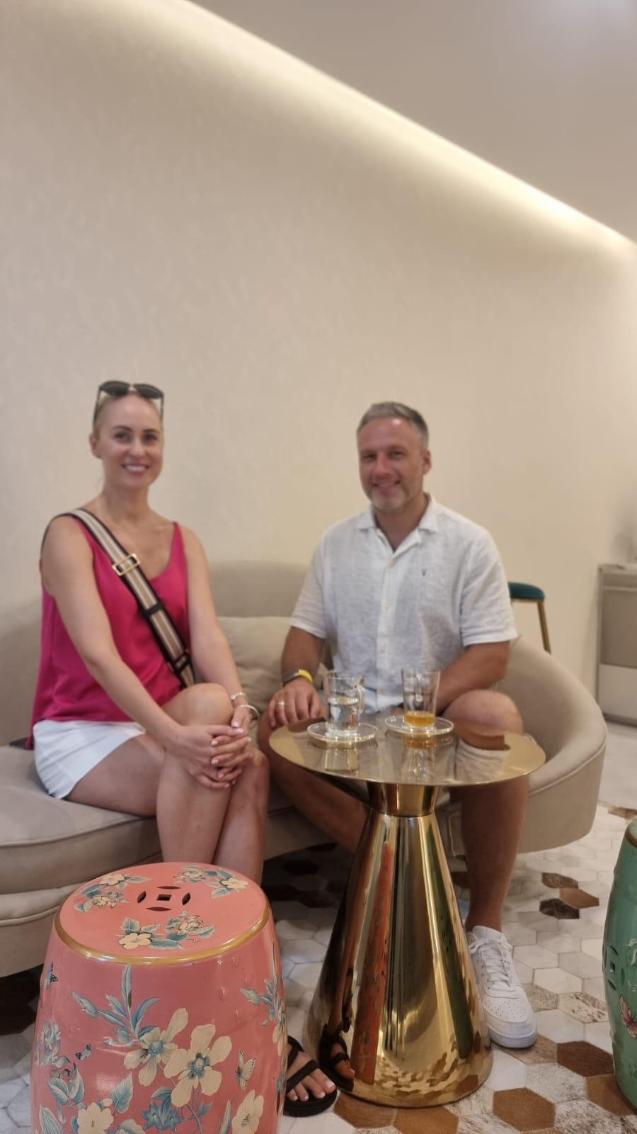 Two guests relaxing on the curved sofa in The Longevity Science Centrum's consultation lounge, with tea served on a gold side table.